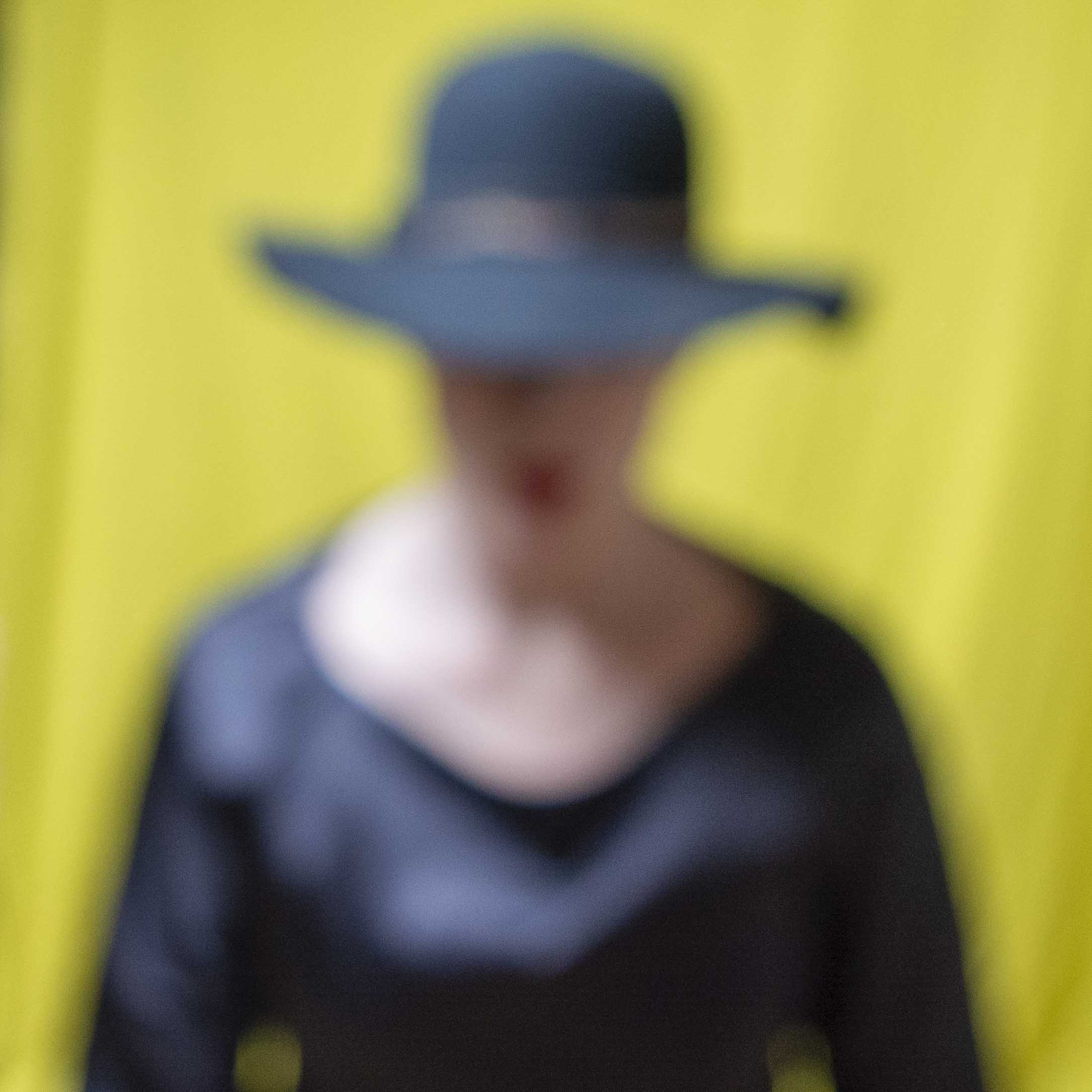Colour Portrait of a woman in a wide brim black hat and black cocktail dress. The background is olive green.